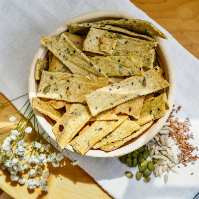 Bowl of crackers on a wooden surface with a white napkin and small flowers.