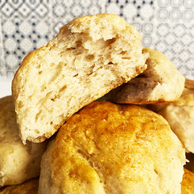 A stack of golden-brown gluten-free dinner rolls, with one roll cut in half to show the soft texture.