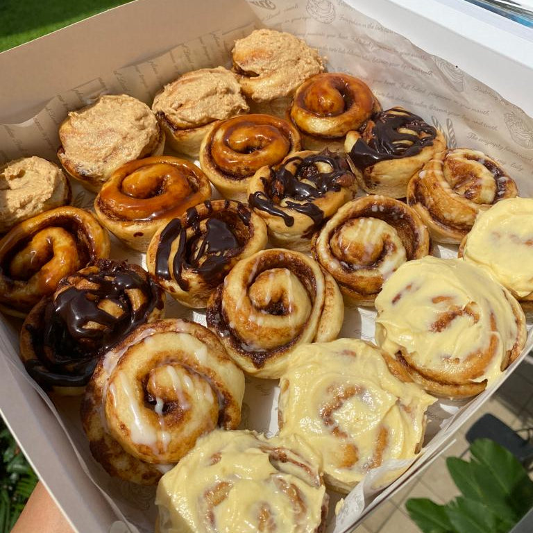 A box of assorted mini cinnamon rolls with different toppings, including glaze, salted caramel, lemon cream cheese, and chocolate.